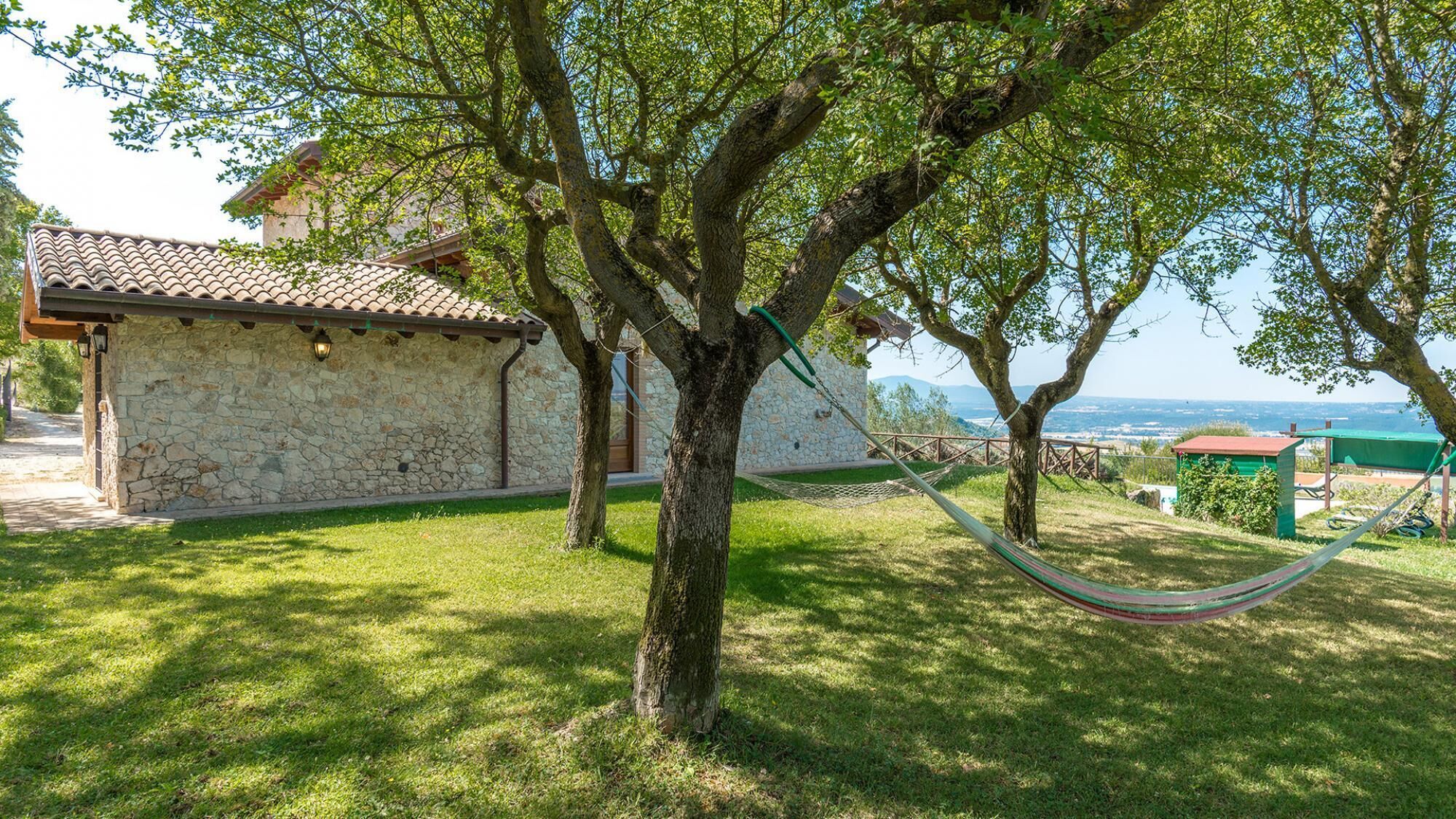 A stone building with a tiled roof, surrounded by lush green grass and trees.