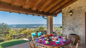 A wooden pergola with a stone wall and a table set for dining with a view of the countryside. - Il Casale Del Nonno 8 2 (Guardea)
