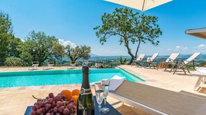 A poolside area with lounge chairs, a table with a bottle and glasses, and a view of the landscape.