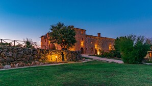 A stone building with a paved pathway leading to the entrance, surrounded by a stone wall and greenery. - Santa Illuminata 20 12 (Massa Martana)