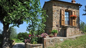 A stone building with a small balcony, potted flowers, and a tree in the foreground. - Monterzi 4 in San Giovanni d Asso (Montalcino)