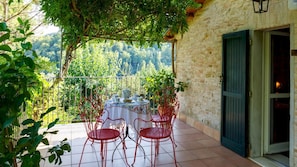 A terrace with a table set for four, surrounded by red chairs, overlooking a forested hillside.