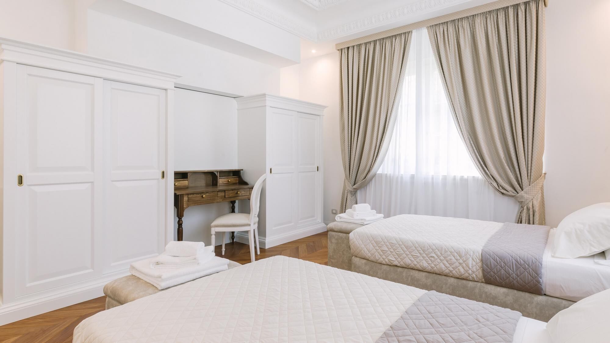 A hotel room with two beds, a desk, and a chair.