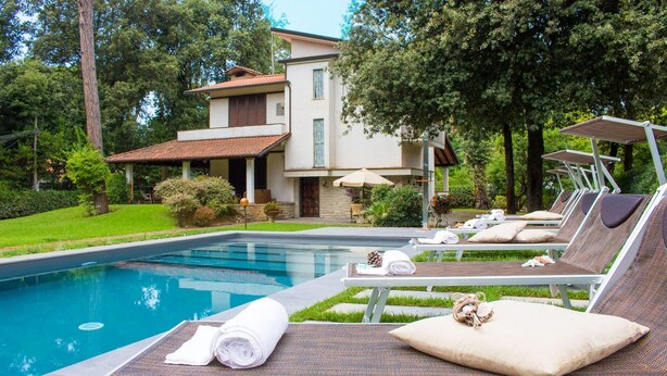 A pool area with lounge chairs and a house in the background.