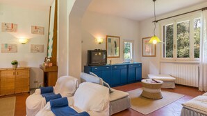 A cozy living room with a sofa, a blue cabinet, a television, and a window with curtains.