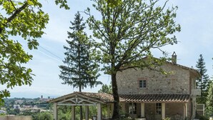 A stone building with a tiled roof, a covered patio, and a view of a town in the background. - Villa La Corte 6 in Montecastrilli (Montecastrilli)