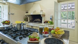 A kitchen with a wood-fired oven, a gas stove, and various fruits and vegetables on the counter. - Villa La Corte 6 in Montecastrilli (Montecastrilli)