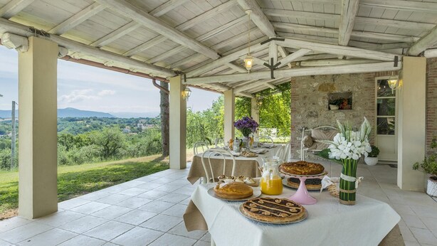 A covered outdoor dining area with a table set for a meal, overlooking a scenic landscape. - Villa La Corte 6 in Montecastrilli (Montecastrilli)