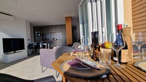 Ein moderner Essbereich mit einem Holztisch, gedeckt für zwei Personen, einem Fernseher und einer Küche im Hintergrund.