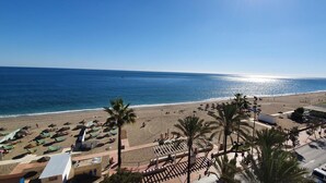 Ein Strand mit Sonnenschirmen, Palmen und einem Parkplatz.