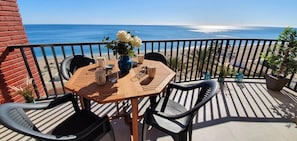 A wooden table with chairs on a balcony overlooking the ocean.
