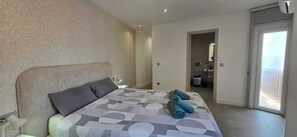 A bedroom with a bed, pillows, and rolled towels. There is a door leading to a bathroom.