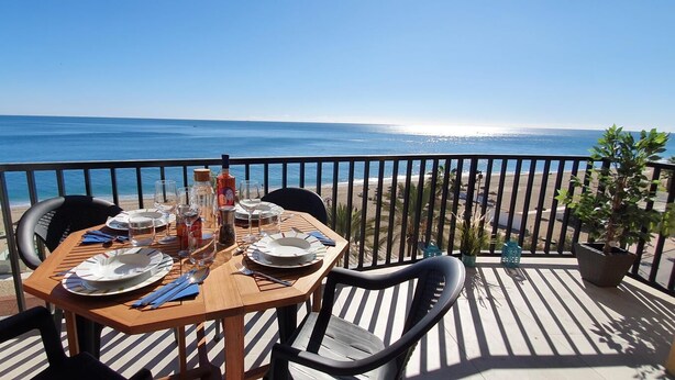Ein Holztisch für zwei Personen gedeckt mit Tellern, Besteck und Gläsern, mit Blick auf einen Strand und den Ozean.