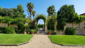 A garden pathway leading to an arched entrance surrounded by lush greenery and potted plants. - Tenuta Di Pratello 24 (Peccioli)