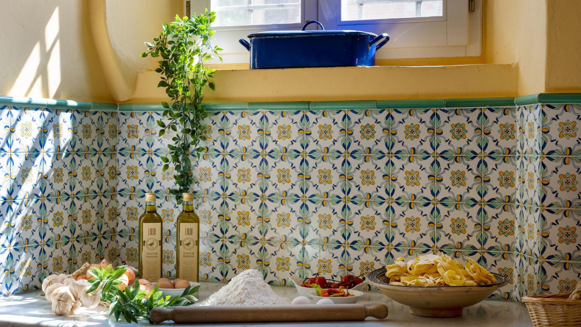 Una cocina con salpicadero de azulejos, una ventana y diversos ingredientes y utensilios de cocina.