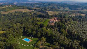 An aerial view of a villa surrounded by dense forest, with a swimming pool and sun loungers in the foreground. - Tenuta Di Pratello 24 (Peccioli)