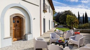 A building with a wooden door and white walls, outdoor seating with tables and chairs, and a garden with a table set for dining. - Torre Angelina 10 2 (Montecatini Terme)