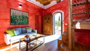 A room with a red wall, a wooden door, a sofa, and a staircase.