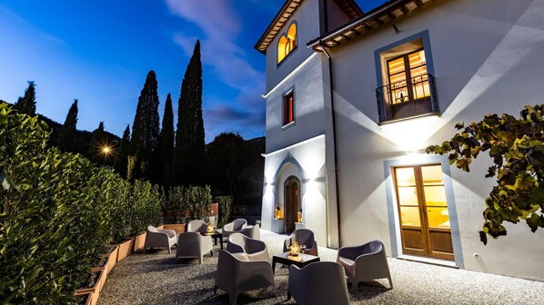 A two-story building with a patio area featuring outdoor seating and a view of tall trees. - Torre Angelina 10 2 (Montecatini Terme)