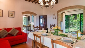 Un coin repas avec une table dressée pour quatre personnes, un canapé rouge et une vue sur la verdure à l’extérieur.
