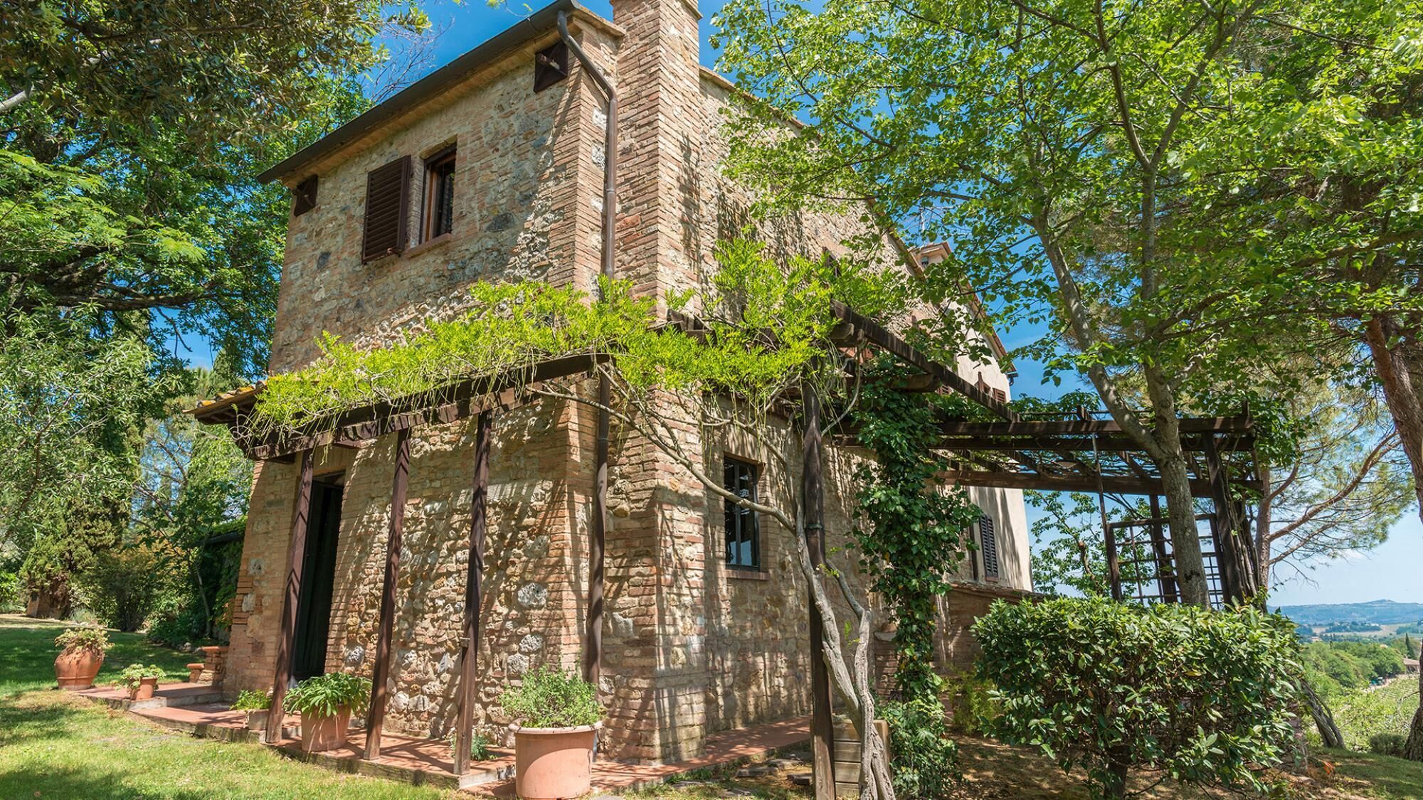 A rustic stone building with a wooden porch, surrounded by lush greenery and trees.