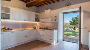 A kitchen with white cabinets, a tiled backsplash, and a view of the outdoors through a glass door.