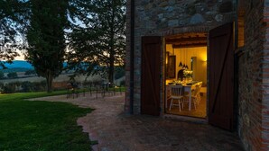 An outdoor dining area with a brick wall and wooden shutters, a table set for dining, and a view of the countryside.