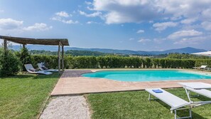 Ett poolområde med en pergola, solstolar och utsikt över bergen.