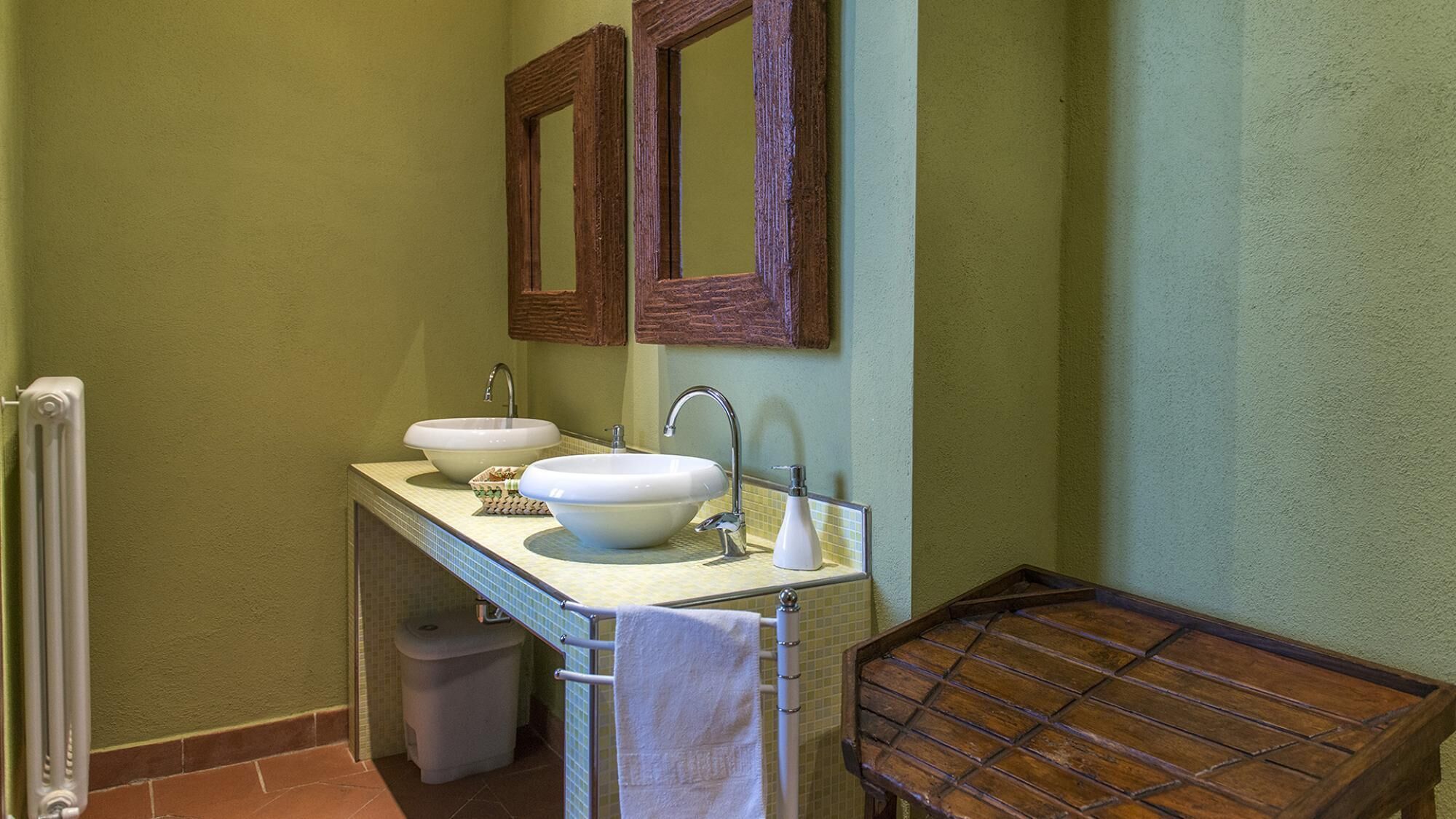 Une salle de bain avec deux lavabos, un miroir et un banc en bois.