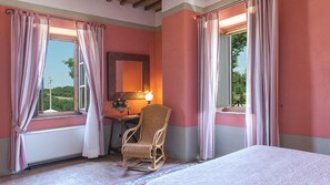 Un dormitorio con paredes rosas, una cama, una silla, un escritorio con lámpara y una ventana con cortinas.