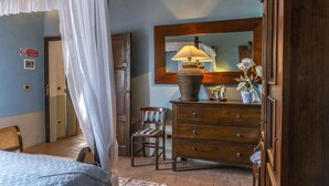 Ein Schlafzimmer mit einem Bett, einer Holzkommode, einem Stuhl, einem Spiegel und einer Lampe.