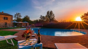 A poolside setting with a table set for two, a bottle of wine, and a glass of red wine. - Podere Sant Eugenio 14 (Chiusdino)