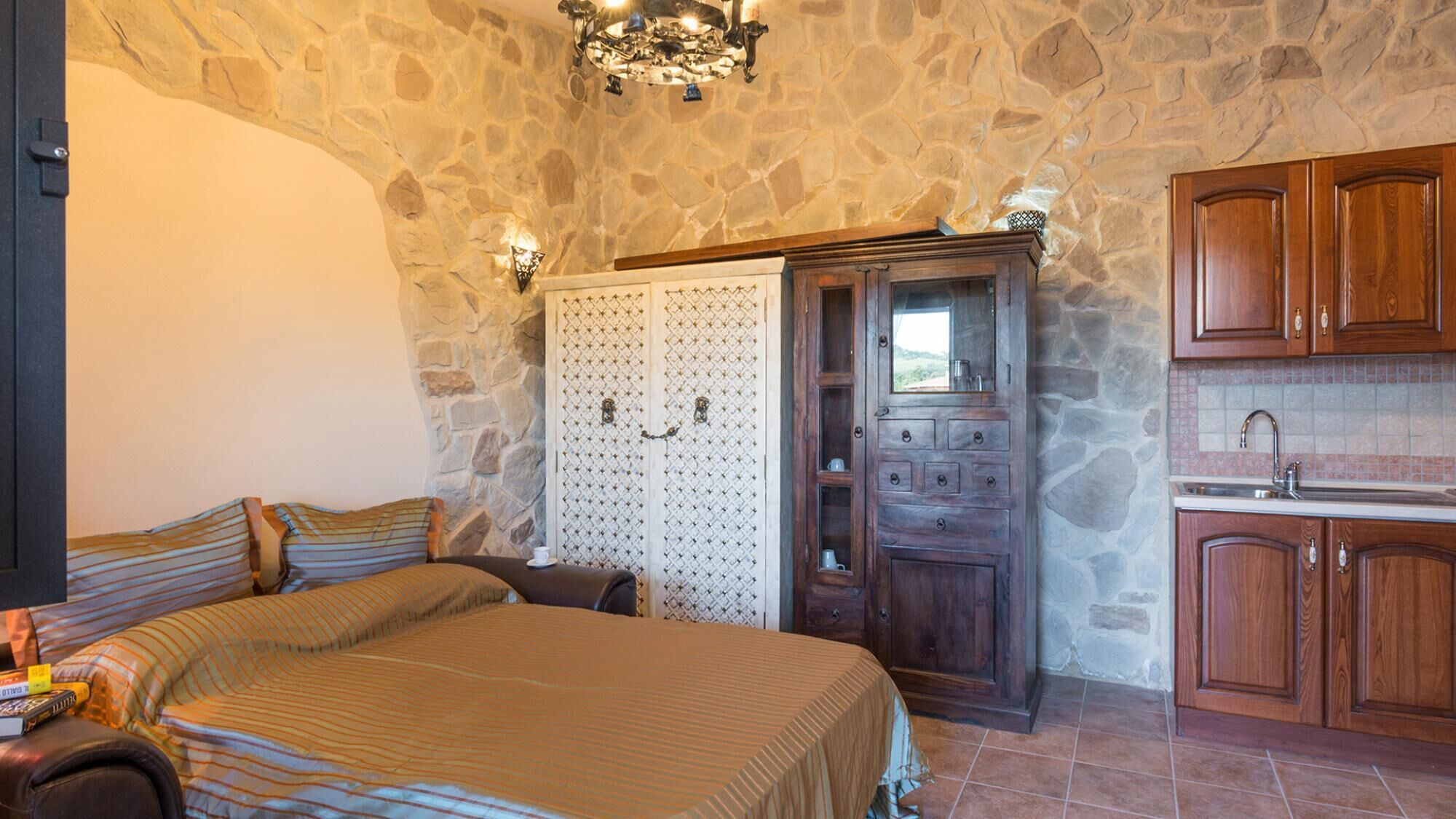 A bedroom with a large bed, a wooden wardrobe, and a stone wall.