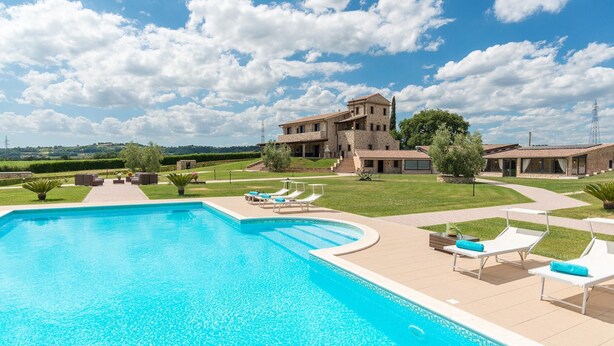 Una gran piscina con tumbonas y un edificio de piedra al fondo.
