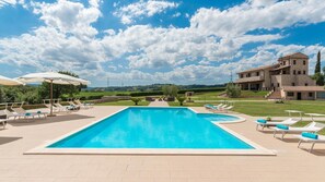 A swimming pool with lounge chairs and umbrellas, surrounded by a landscaped garden and a large building. - Podere Torricella 16 4 (Narni)