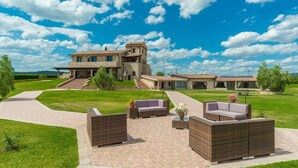Una casa de piedra grande con un patio que tiene mobiliario de mimbre y un camino pavimentado.