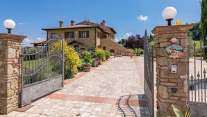 Une maison en pierre avec une allée pavée menant à une entrée fermée par un portail.