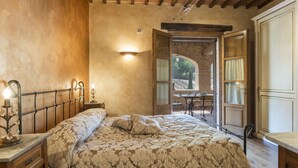 Une chambre à coucher comprenant un lit, une table de chevet, une lampe et une porte ouverte donnant sur un balcon avec une table et des chaises.