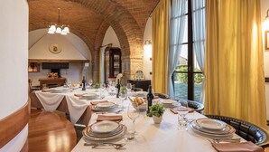 A dining area with a brick arch ceiling, large windows with yellow curtains, and a table set for a meal. - Villa Siena 10 in Castelnuovo Berardenga (Castelnuovo Berardenga)
