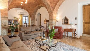 A cozy living room with a brick archway, a sofa, a glass coffee table, and a red armchair. - Villa Siena 10 in Castelnuovo Berardenga (Castelnuovo Berardenga)