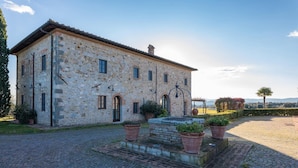 A stone building with a tiled roof, a courtyard with potted plants, and a view of the surrounding landscape. - Villa Siena 10 in Castelnuovo Berardenga (Castelnuovo Berardenga)