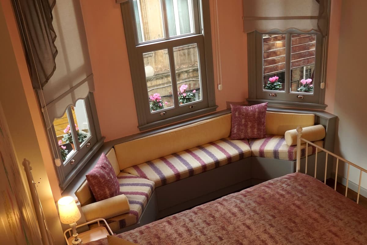 A bedroom with a large bed, a bench seat, and a window with curtains.