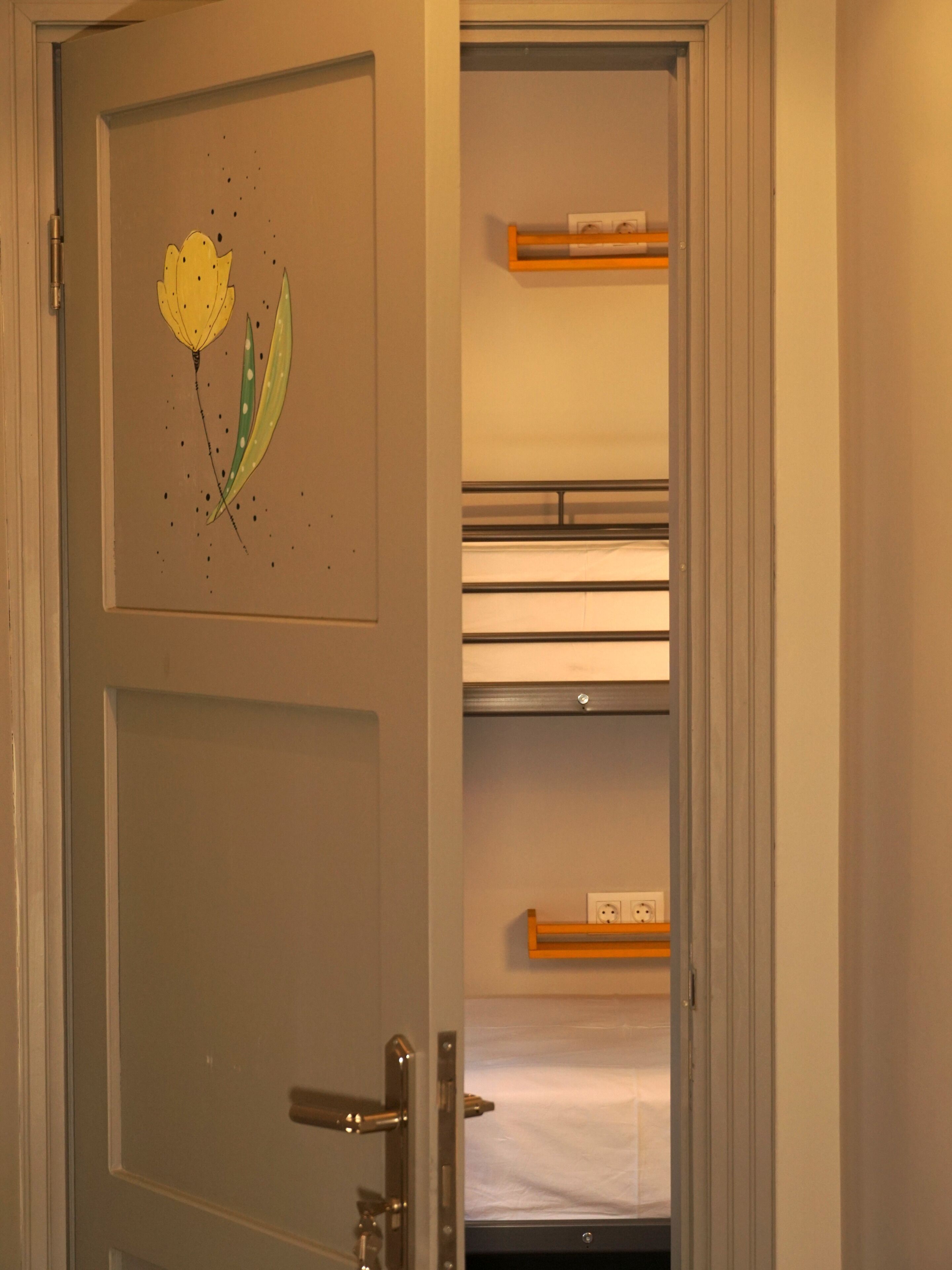 Une pièce avec une porte ornée d’un autocollant décoratif, un lit recouvert d’un drap blanc et une étagère sur laquelle se trouve un petit objet.