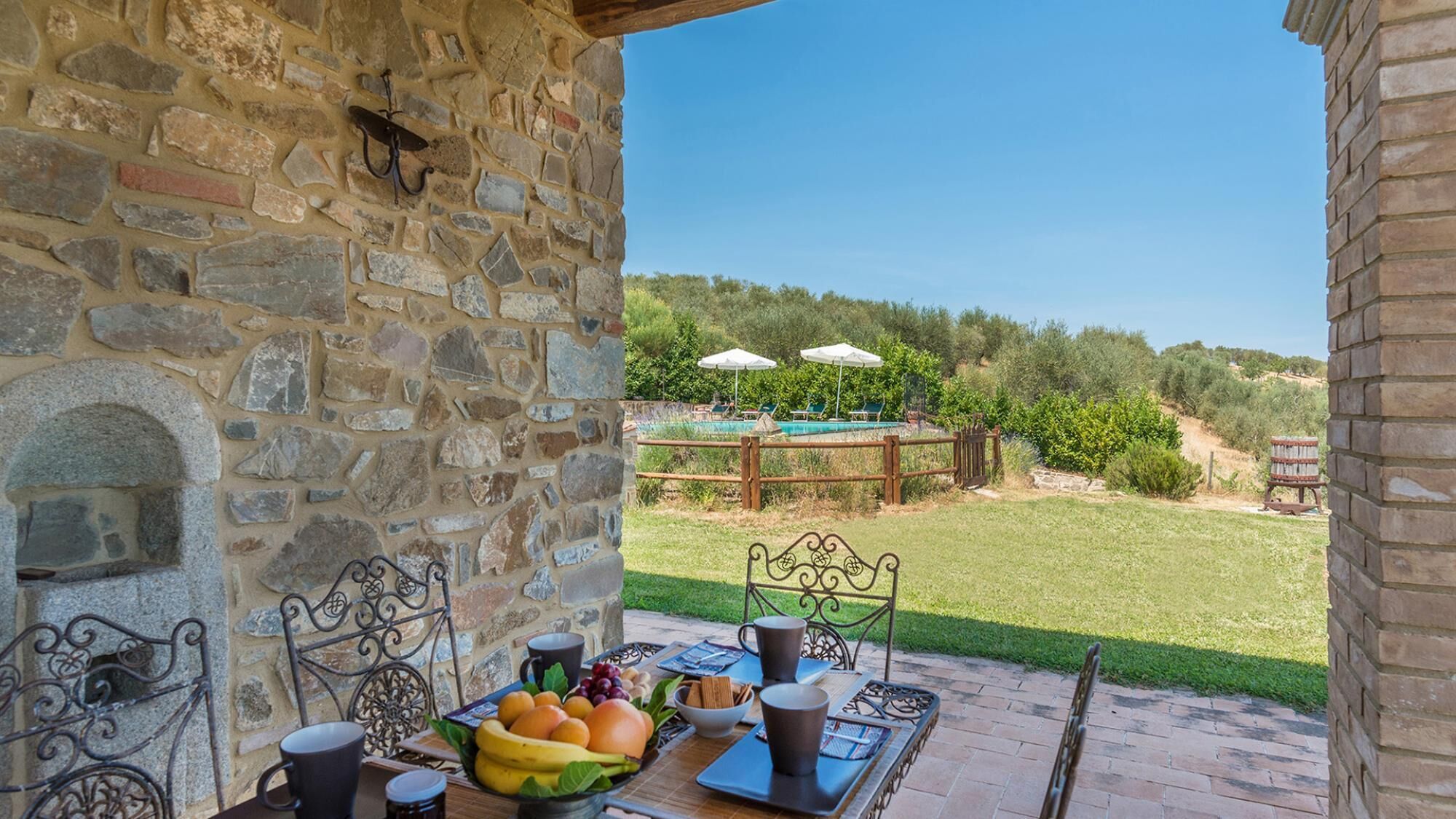 Un patio de piedra con una mesa dispuesta para el desayuno, con vista a una piscina y exuberante vegetación.