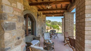 A stone-walled patio with wicker furniture, a table, and a view of the countryside. - Le Macine 6 in Castel del Piano (Castel del Piano)