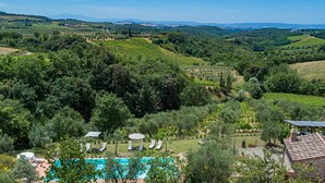 A vineyard landscape with a swimming pool, lounge chairs, and a small building. - Villa Santa Maria 14 (Castelnuovo Berardenga)
