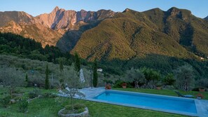 A swimming pool surrounded by a garden with a view of mountains.