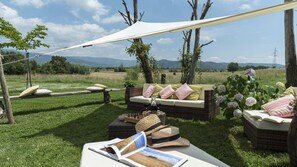 An outdoor seating area with wicker furniture, cushions, and a table with a book and a hat.