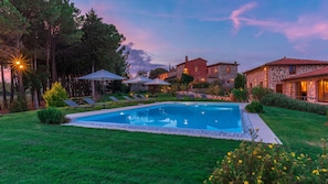 A swimming pool surrounded by a well-maintained lawn, with lounge chairs and umbrellas.