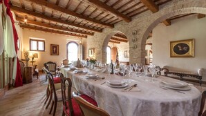 Una larga mesa de comedor lista para una comida en una habitación rústica con vigas de madera a la vista y paredes de piedra.